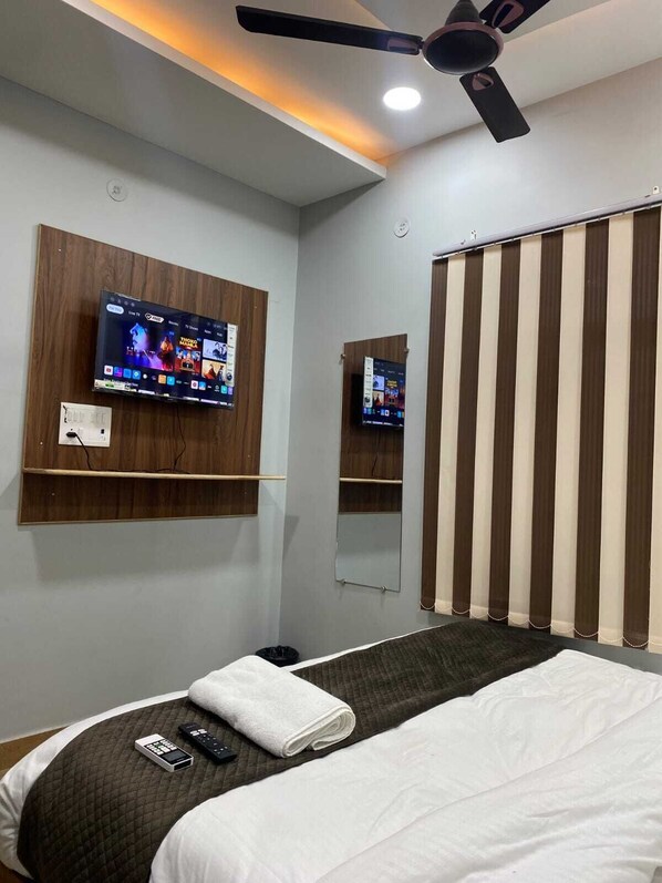 Habitación de hotel con cama, televisión montada en la pared, ventilador de techo y ventana con cortinas.