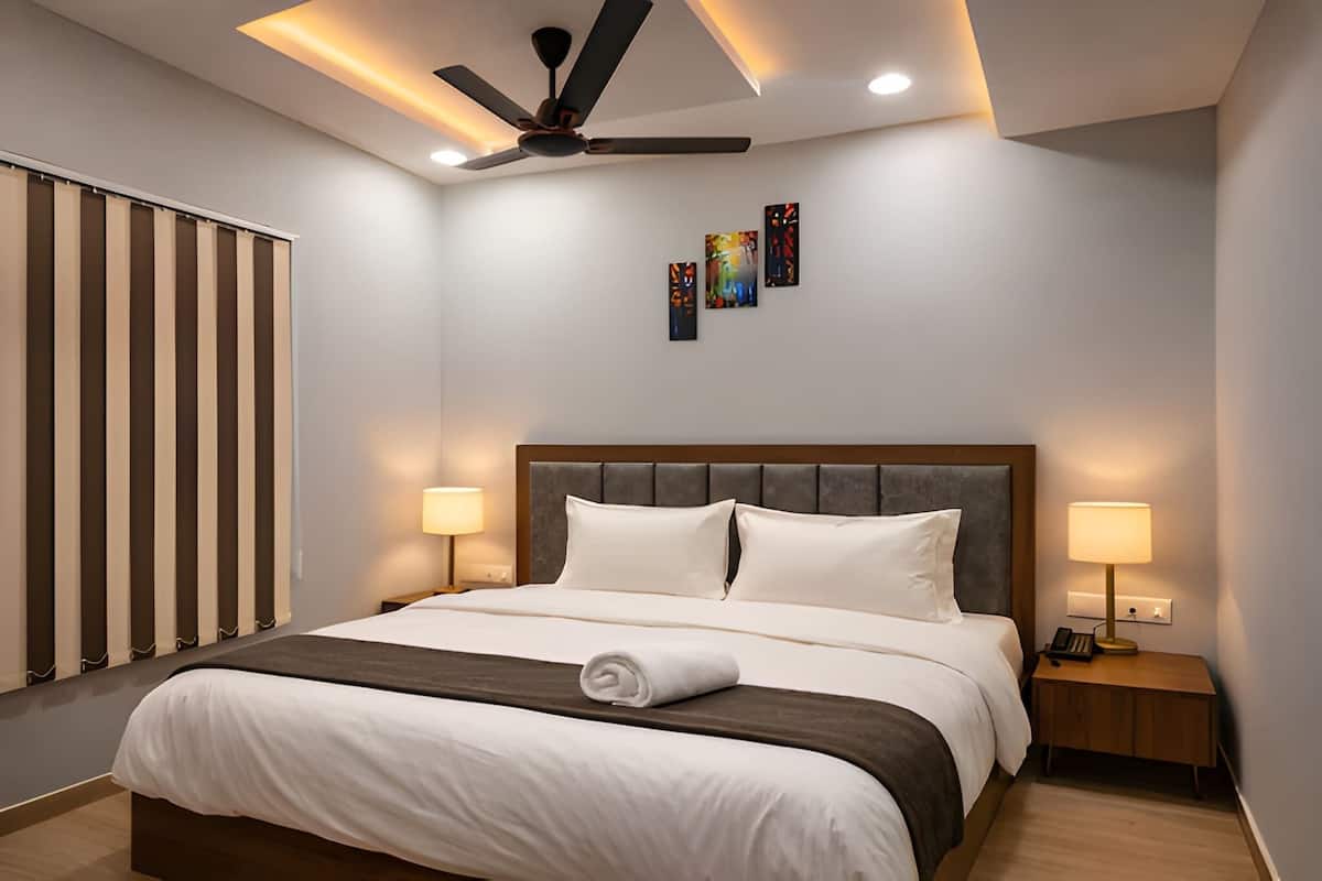 A hotel room with a bed, bedside lamps, a ceiling fan, and artwork on the wall.