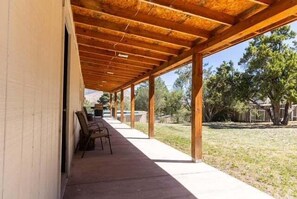 Un portico coperto con tetto in legno, pavimento in cemento e vista su un prato alberato.