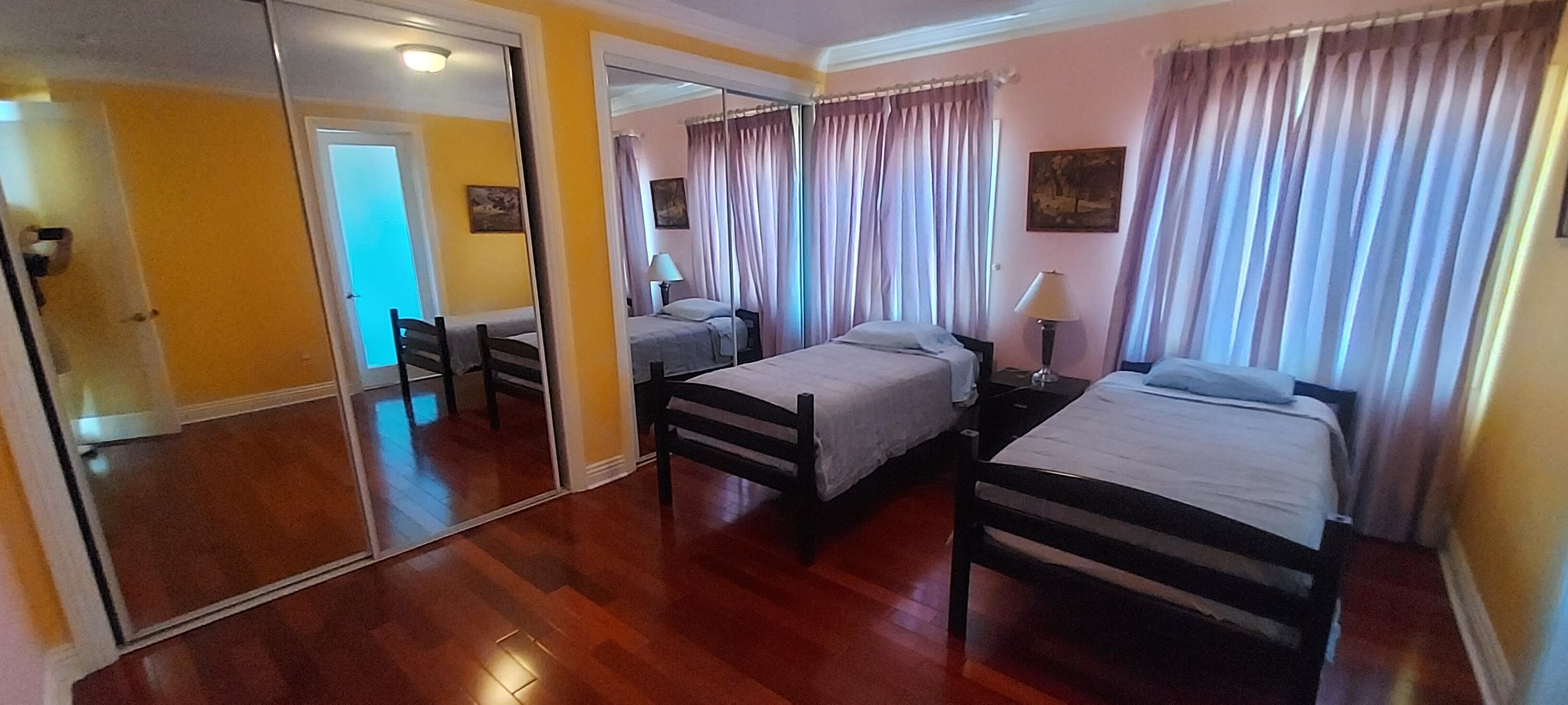 Ein Hotelzimmer mit zwei Einzelbetten, Holzboden, einem großen Spiegel und einer Tür zu einem weiteren Raum.