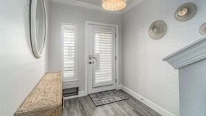 A hallway with a wooden bench, a door with white blinds, a textured ceiling light, and decorative wall plates. - Waterfront Townhome w/ Garage – St. Pete (St. Petersburg)