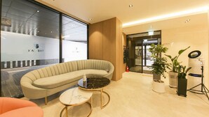 A modern reception area with a curved sofa, a small round table, and potted plants. - Gimhae The Van Hotel (Gimhae)