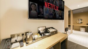 A hotel room with a flat-screen TV displaying Netflix content, a minibar, a telephone, and a wooden desk. - Gimhae The Van Hotel (Gimhae)
