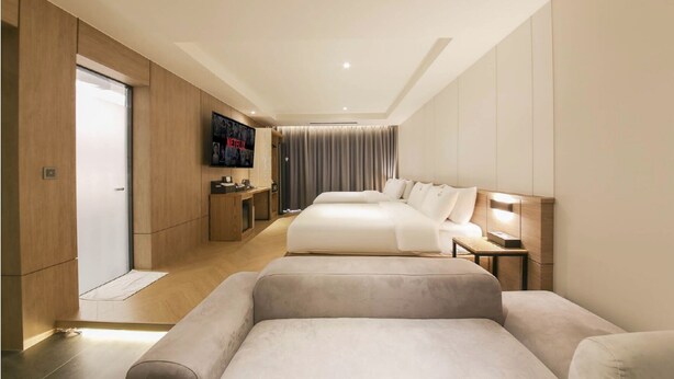 A modern hotel room with a large bed, a smaller sofa, a desk with a chair, a TV mounted on the wall, and a sliding door. - Gimhae The Van Hotel (Gimhae)
