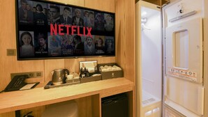 A hotel room with a flat-screen TV displaying a Netflix interface, a wooden desk with a coffee maker, a remote control, and a small box of toiletries. - Gimhae The Van Hotel (Gimhae)
