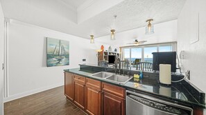 Una cocina con una isla grande, armarios de madera, un lavavajillas de acero inoxidable y vista al océano a través de amplios ventanales.
