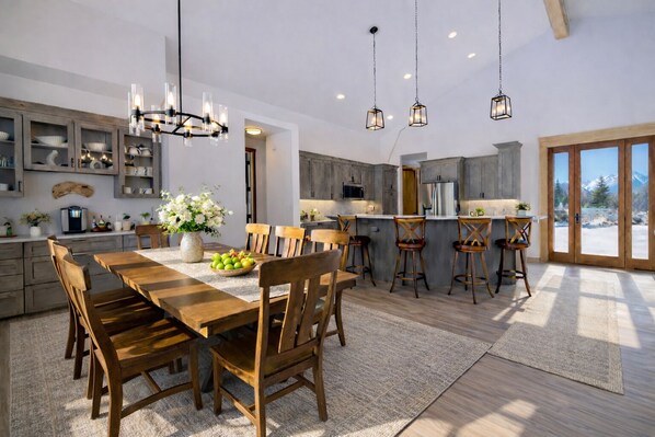 Una cocina moderna con armarios de madera, un comedor con una mesa grande y sillas, y vistas a montañas a través de puertas corredizas de vidrio.
