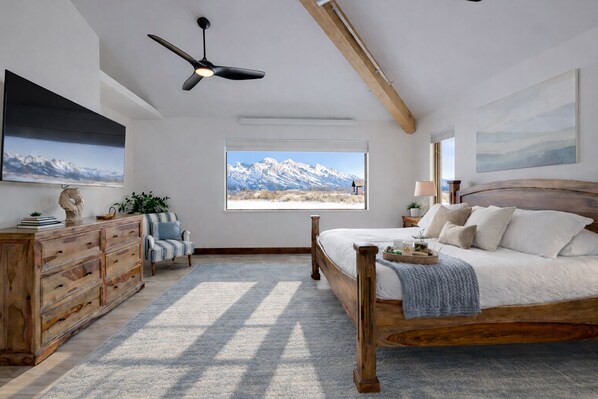A bedroom with a wooden bed, a dresser, a chair, a TV, and a window with a mountain view. - Brand New Luxury Estate by Jackson Hole Rentals™ (Jackson)