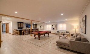 A spacious living room with a pool table, a sofa, and a bar area with a TV. - Brand New Luxury Estate by Jackson Hole Rentals™ (Jackson)