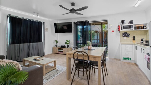Ein modernes Wohnzimmer mit Sofa, Couchtisch und Fernseher. Es beinhaltet einen Essbereich mit Tisch und Stühlen sowie eine Küche mit Schränken und Geräten.