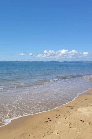 Una spiaggia con acque cristalline, una battigia sabbiosa e montagne in lontananza.