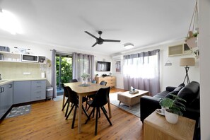 A modern kitchen with a dining area, a living room with a sofa, and a TV. - Saltwater Sunset - Relax by the Ocean (East Mackay)