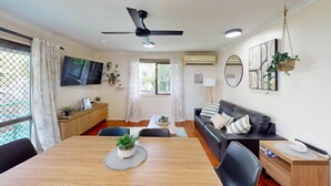 A modern living room with a wooden dining table, black leather sofa, and a ceiling fan. - Saltwater Sand - relax by the beach (East Mackay)