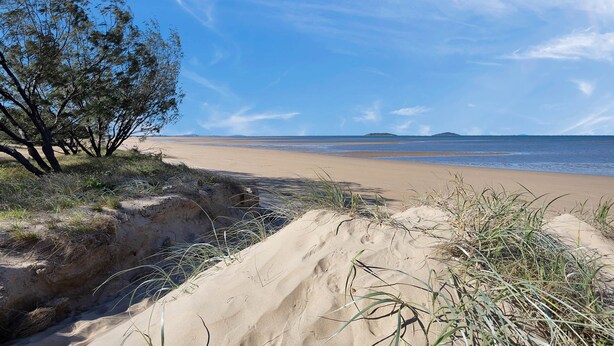A beach with sand dunes, sparse vegetation, and a clear blue sky. - Saltwater Sand - relax by the beach (East Mackay)