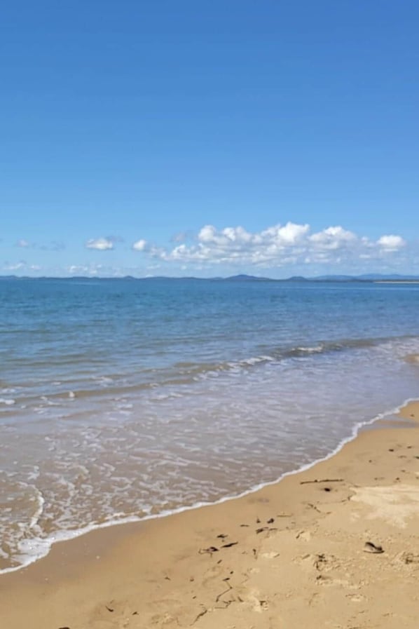 A beach with clear water, a sandy shore, and distant mountains.