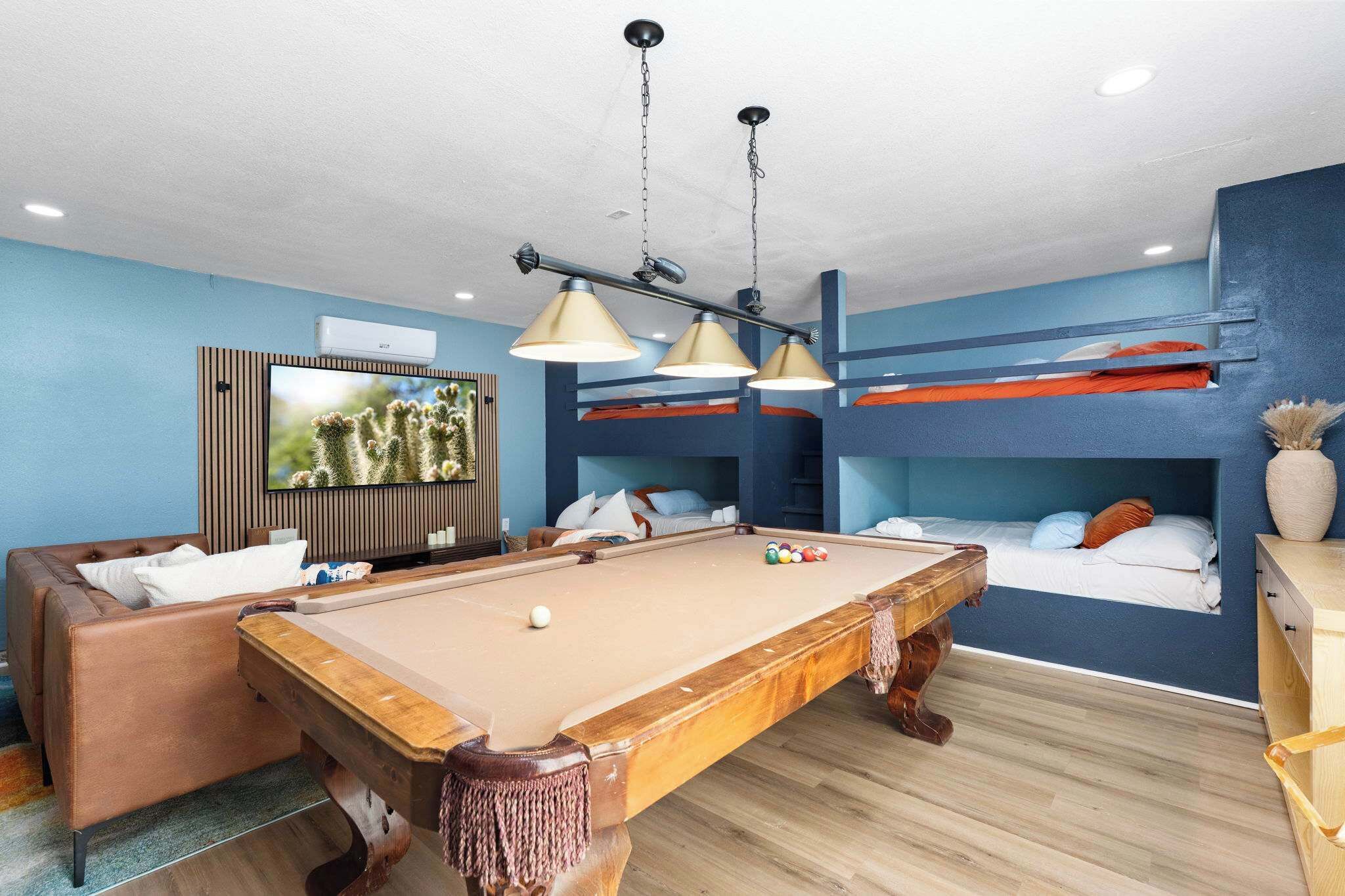 A pool table in a room with bunk beds, a sofa, and a television.
