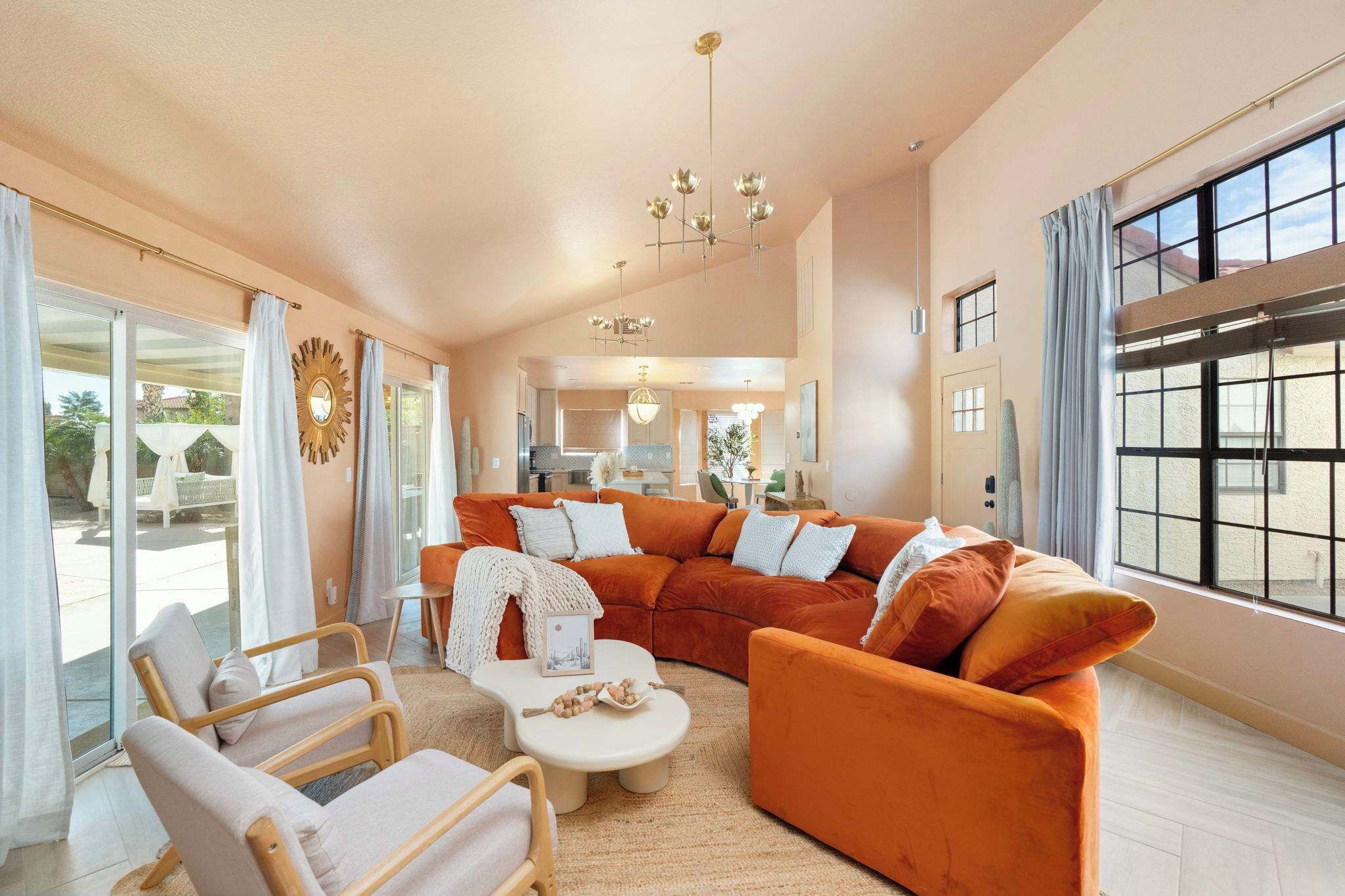 A spacious living room with a large orange sectional sofa, a wooden coffee table, and a glass door leading to an outdoor area.