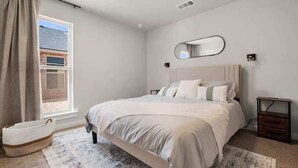 A bedroom with a large bed, a window with curtains, a bedside table, and a wall-mounted mirror. - Wellness Retreat - 3BR/2BA - Family Friendly (Lubbock)