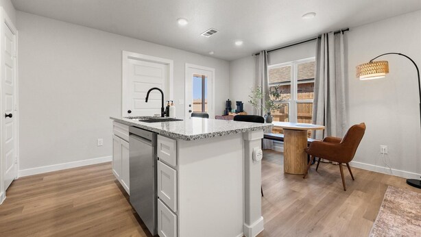 A modern kitchen with white cabinets, a granite countertop, and a built-in dishwasher. There is a dining area with a wooden table and chairs, and a large window with curtains. - Wellness Retreat - 3BR/2BA - Family Friendly (Lubbock)