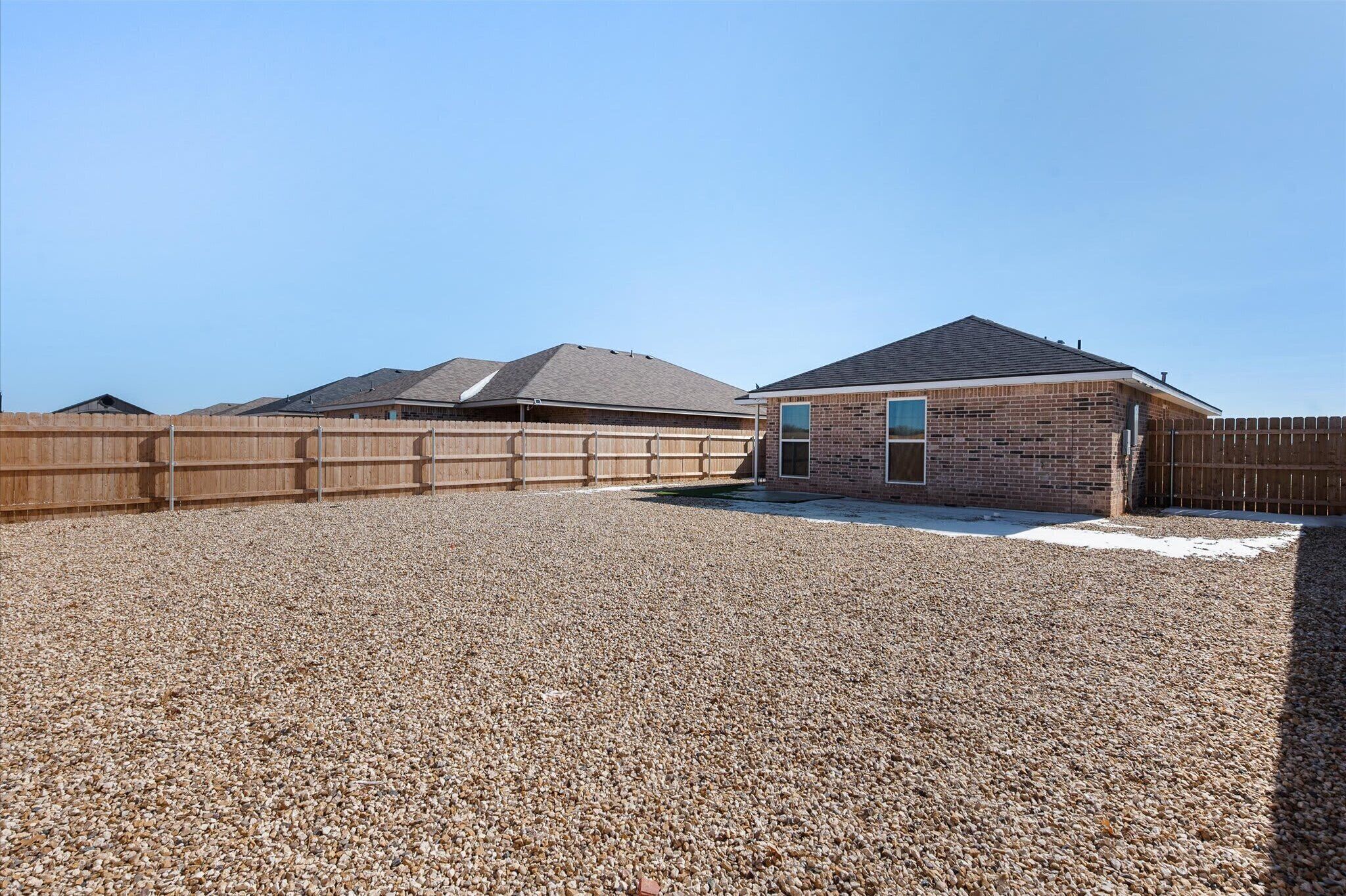 Un barrio residencial con camino de grava, vallas de madera y casas de ladrillo.