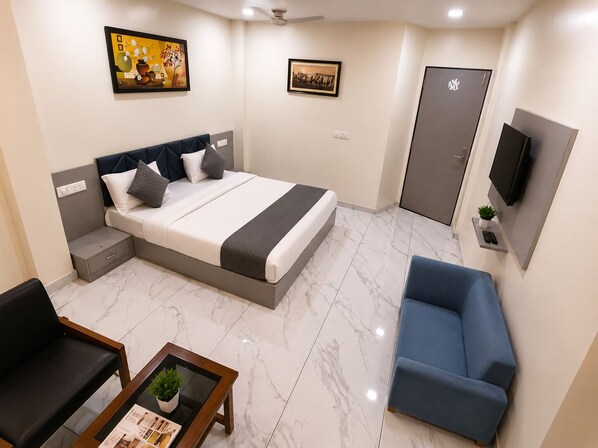 A hotel room with a bed, bedside tables, a sofa, a TV, and artwork on the walls. - Soneva Hotel (Ahmedabad)
