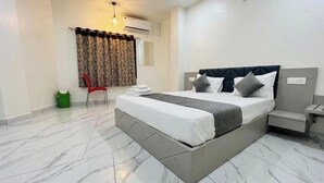 A modern hotel room with a large bed, a chair, a small table, and a trash bin. - Soneva Hotel (Ahmedabad)