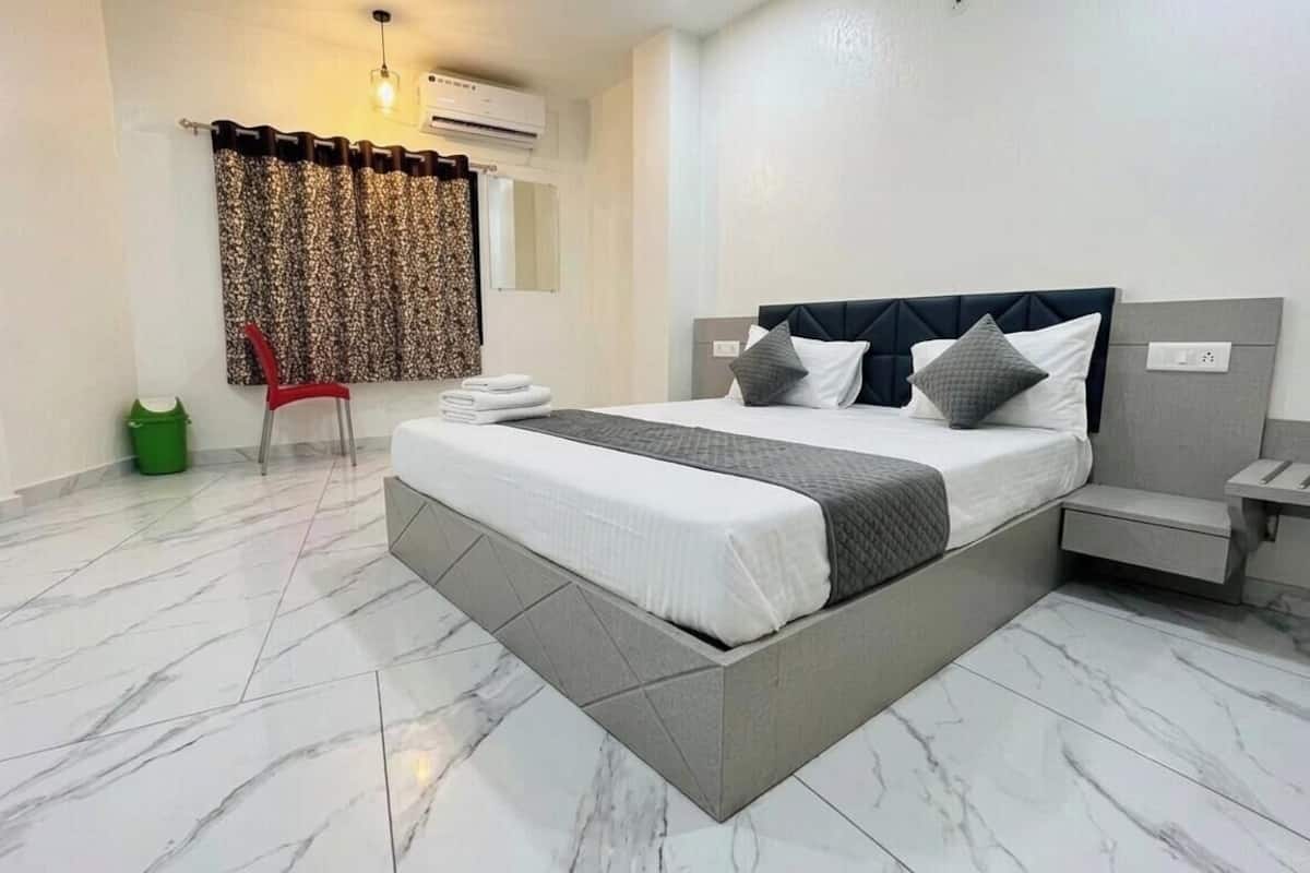 A modern hotel room with a large bed, a chair, a small table, and a trash bin.