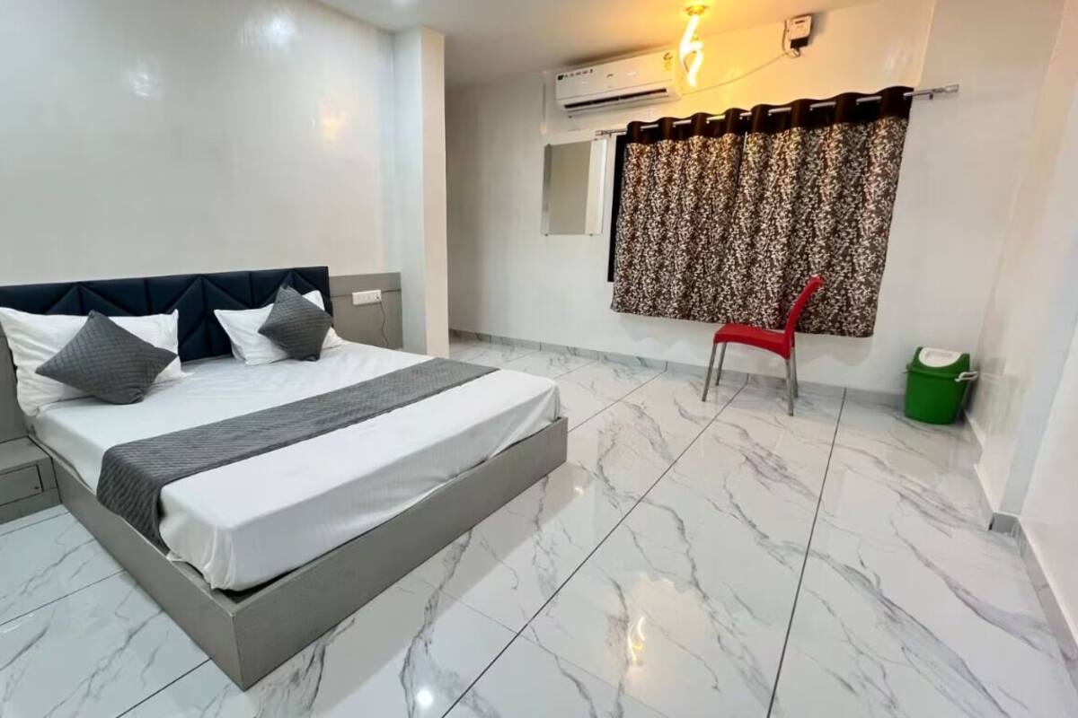 A hotel room with a bed, a chair, a nightstand, and a window with curtains.