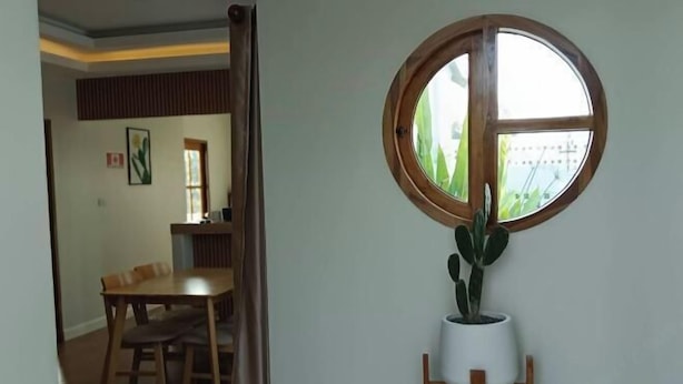 Habitació amb zona de dinar, una planta en test i finestra amb vista a vegetació.
