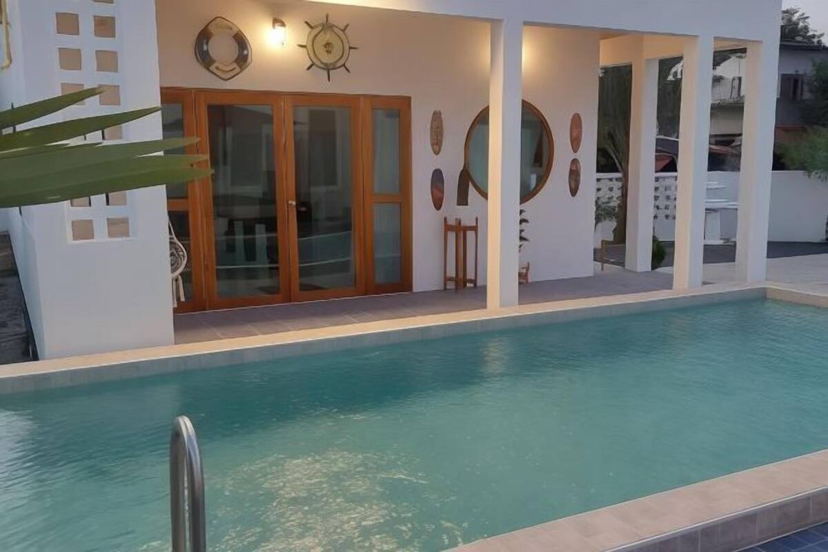Un espace moderne aménagé au bord de la piscine, avec une piscine à eau claire, des portes en bois et des œuvres d’art décoratives sur les murs.