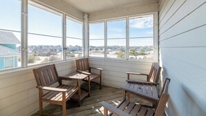 Eine überdachte Veranda mit Holzmöbeln und großen Fenstern, die einen Blick auf die umliegende Landschaft bieten.