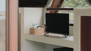 A room with a wooden ceiling, a television on a stand, a small black refrigerator, and a window with a view of greenery. - Limbo Lux Bungalows (Kuta)