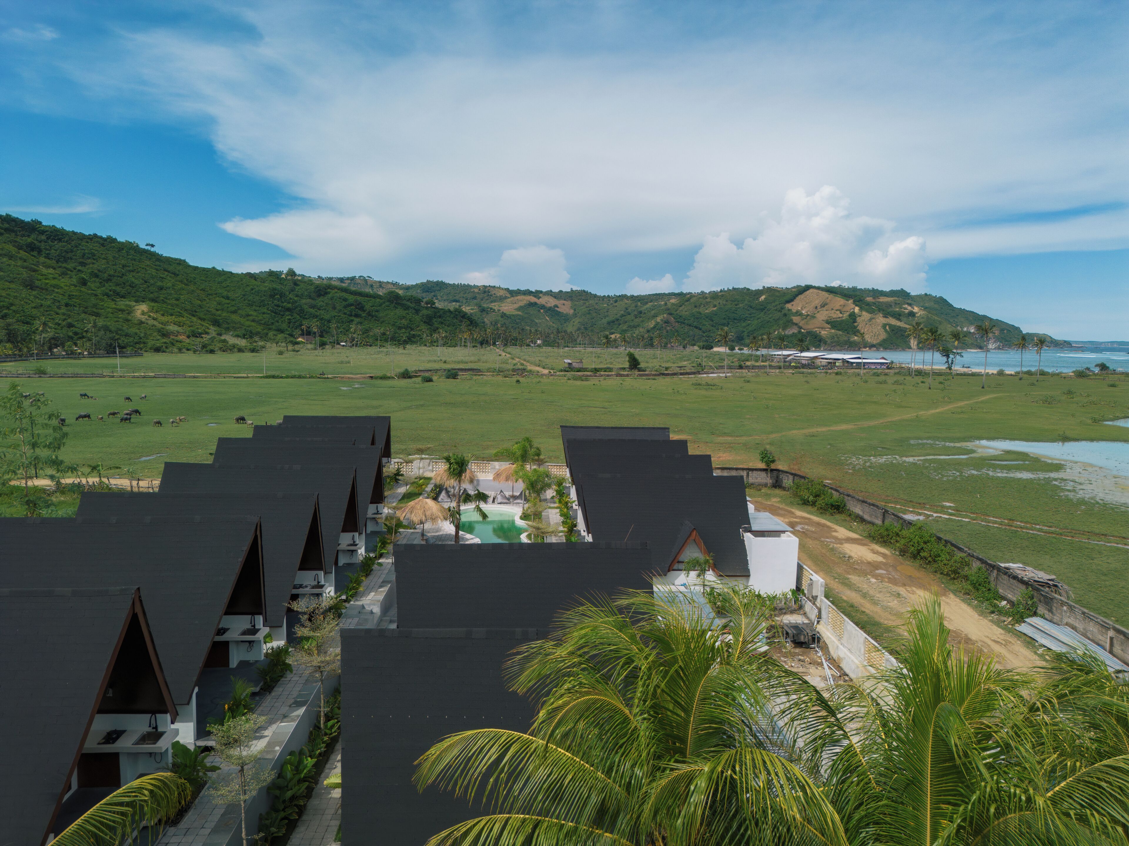 Un resort con varias cabañas, una piscina y vistas del paisaje circundante, incluyendo colinas y una masa de agua.