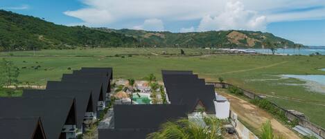 Un resort con varias cabañas, una piscina y vistas del paisaje circundante, incluyendo colinas y una masa de agua.