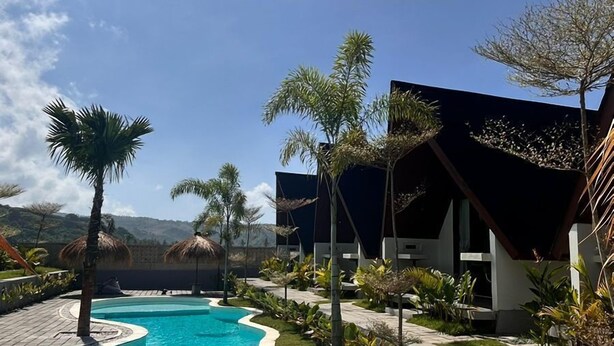 A swimming pool with a curved edge, surrounded by a paved deck. - Limbo Lux Bungalows (Kuta)