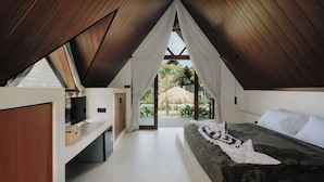 A bedroom with a sloped ceiling, a bed, a TV, and a view of a palm tree. - Limbo Lux Bungalows (Kuta)