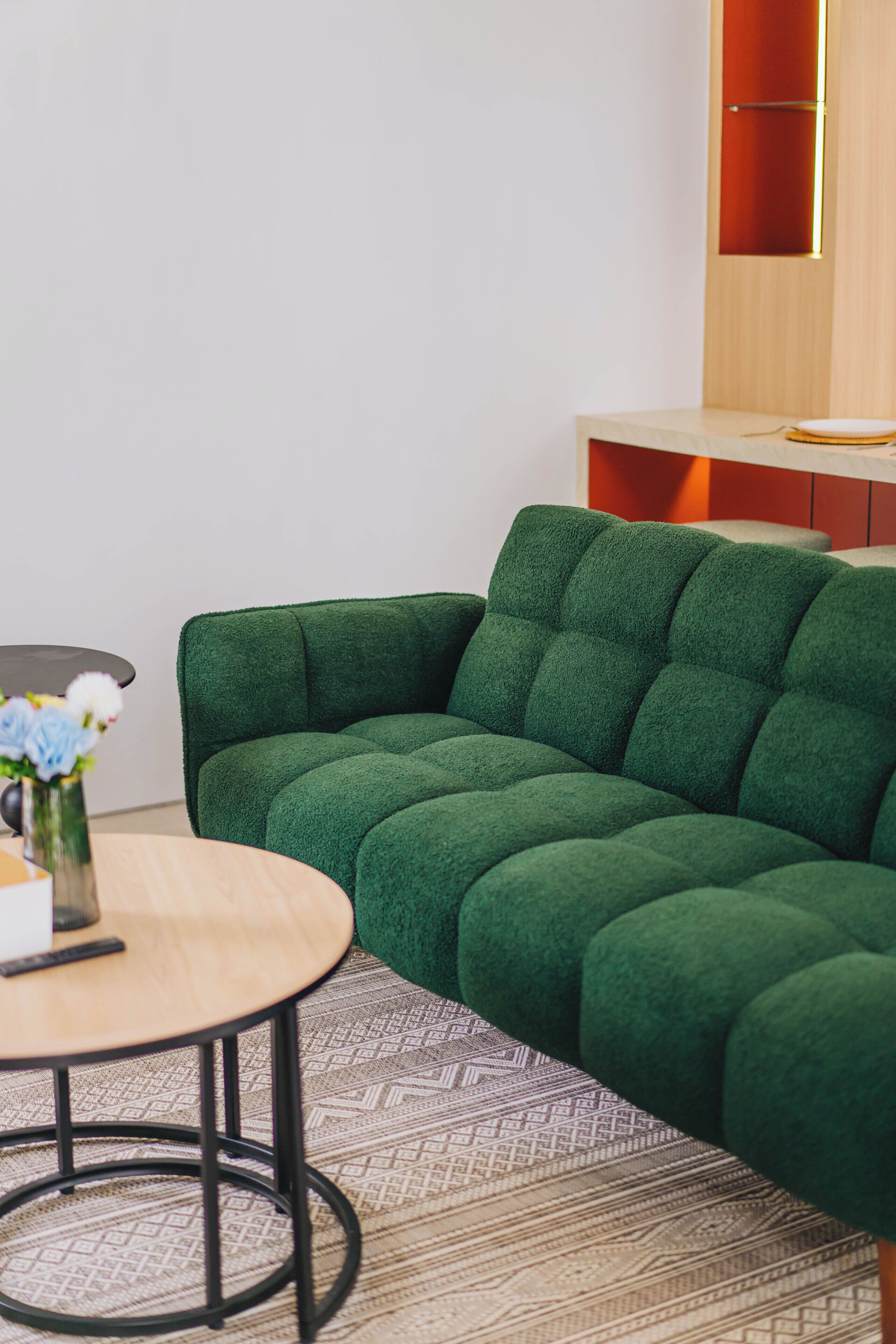 A green sofa, a round table with a vase of flowers, and a patterned rug.