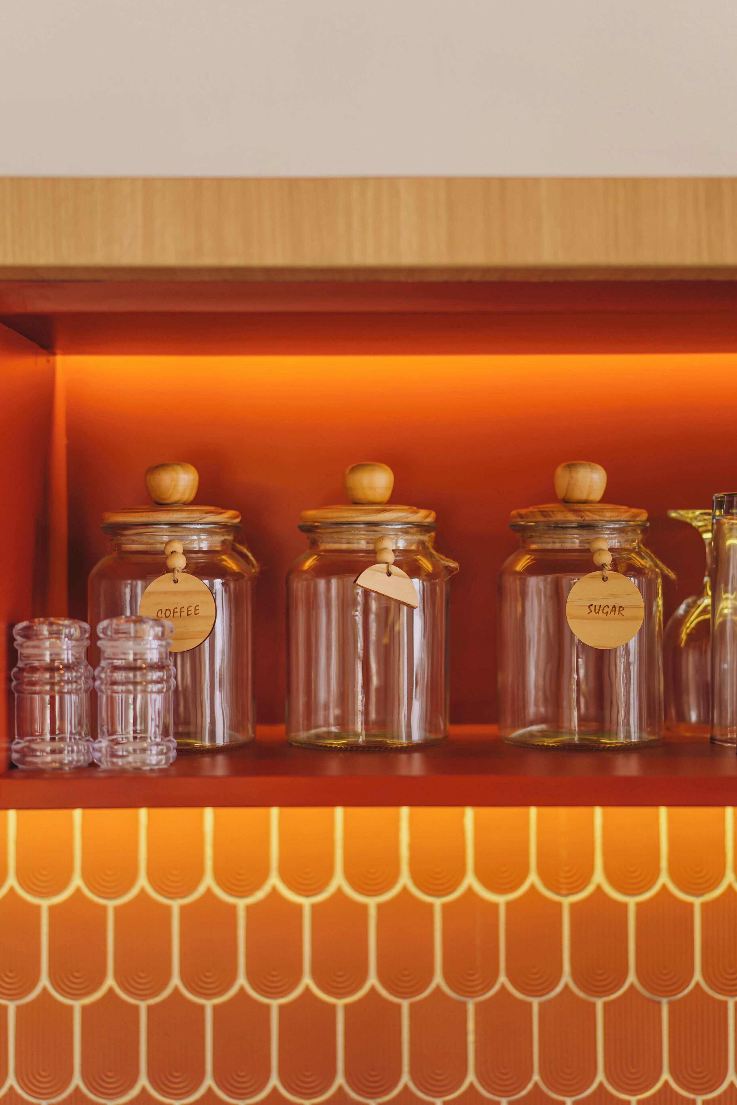 Une étagère avec des bocaux en verre étiquetés « Café » et « Sucre », ainsi que de plus petits récipients en verre.