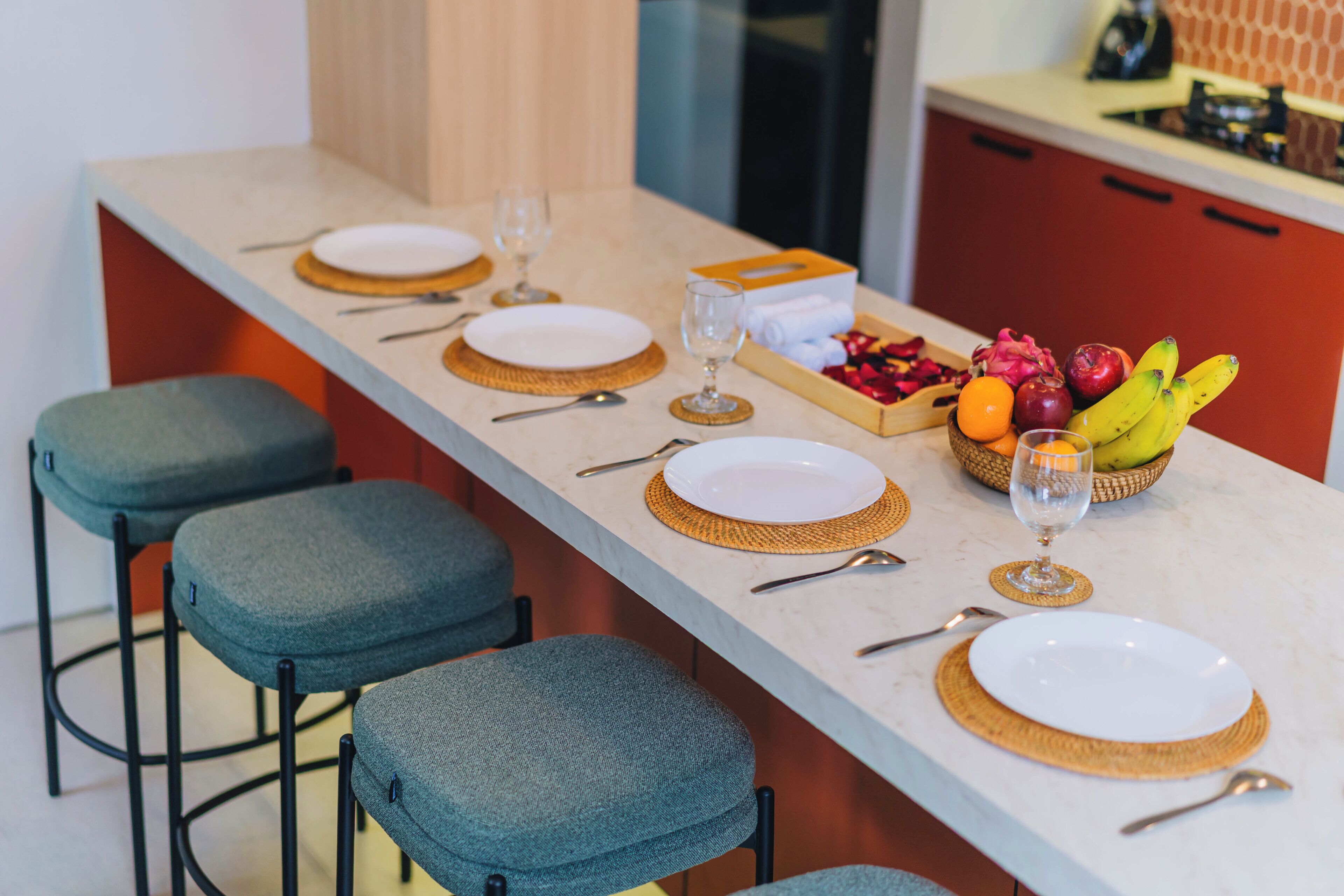 Une cuisine avec un long comptoir, des tabourets de bar et un panier de fruits.
