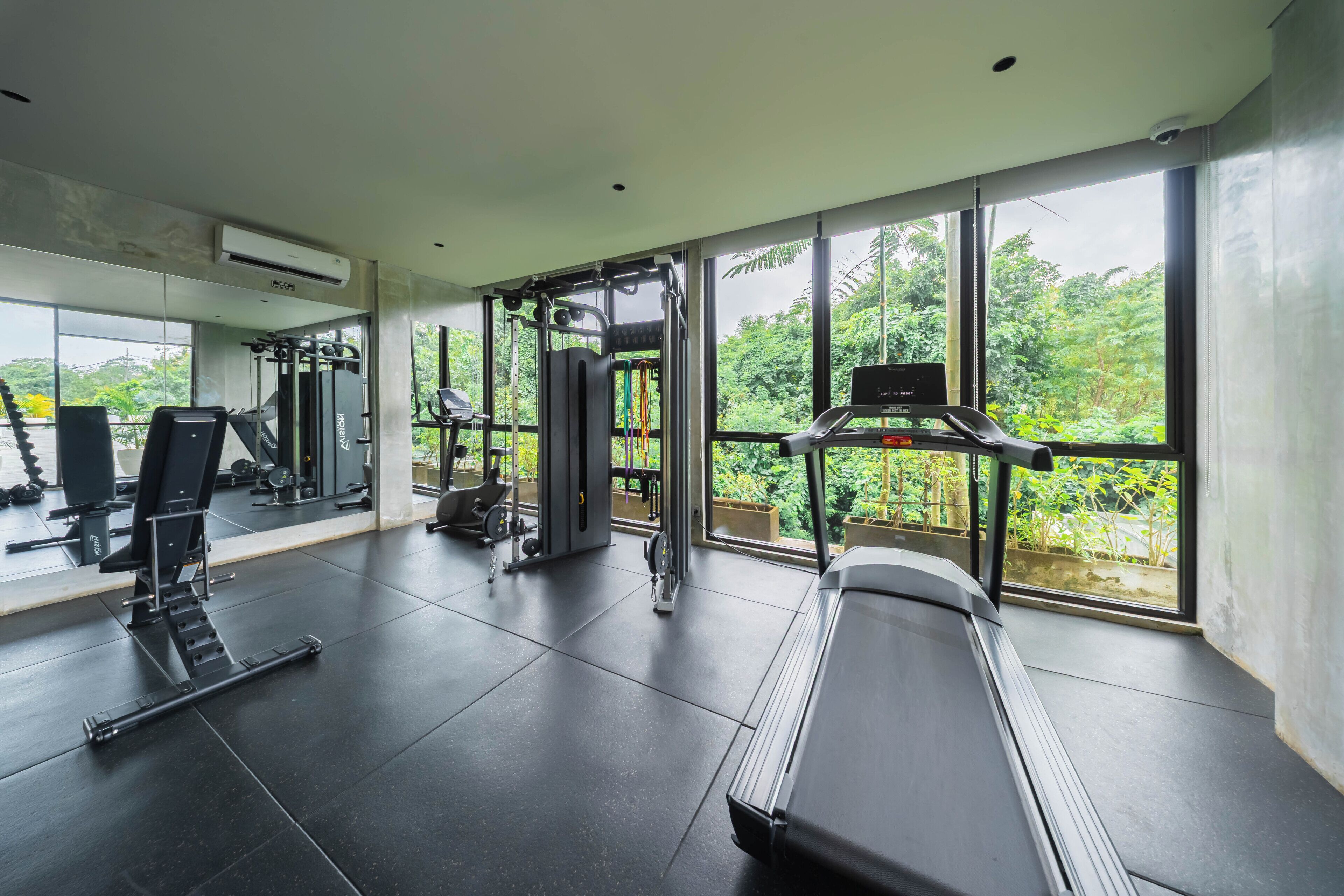 A gym with various exercise equipment, large windows, and a view of greenery.