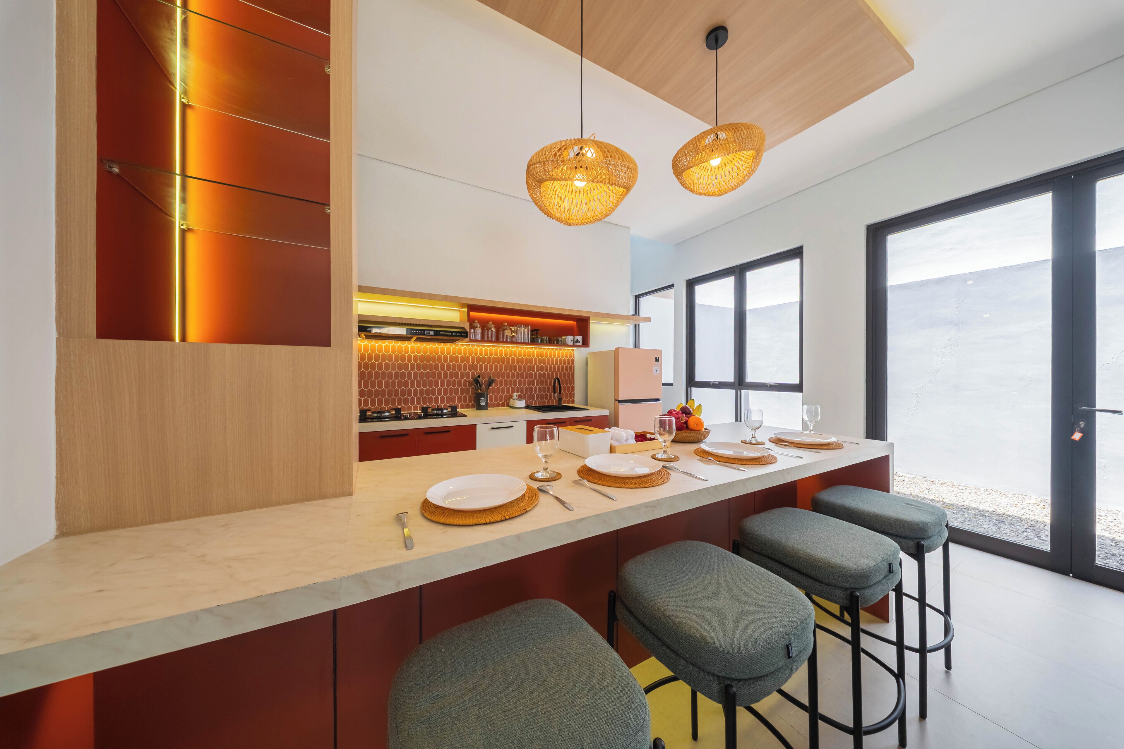 A modern kitchen with a bar area, pendant lights, and a view through large windows.