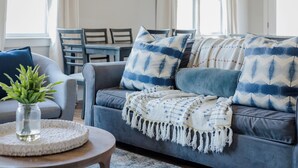 A modern living room with a grey sofa, blue and white patterned pillows, a woven throw blanket, and a small plant on a round wooden table. - 4BR Nashville Stay w/ Pool Table & Patio! (Nashville)