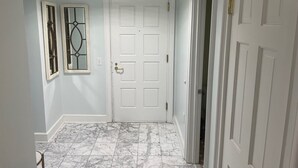 Un pasillo con una puerta blanca, dos ventanas decorativas y un suelo de mármol.