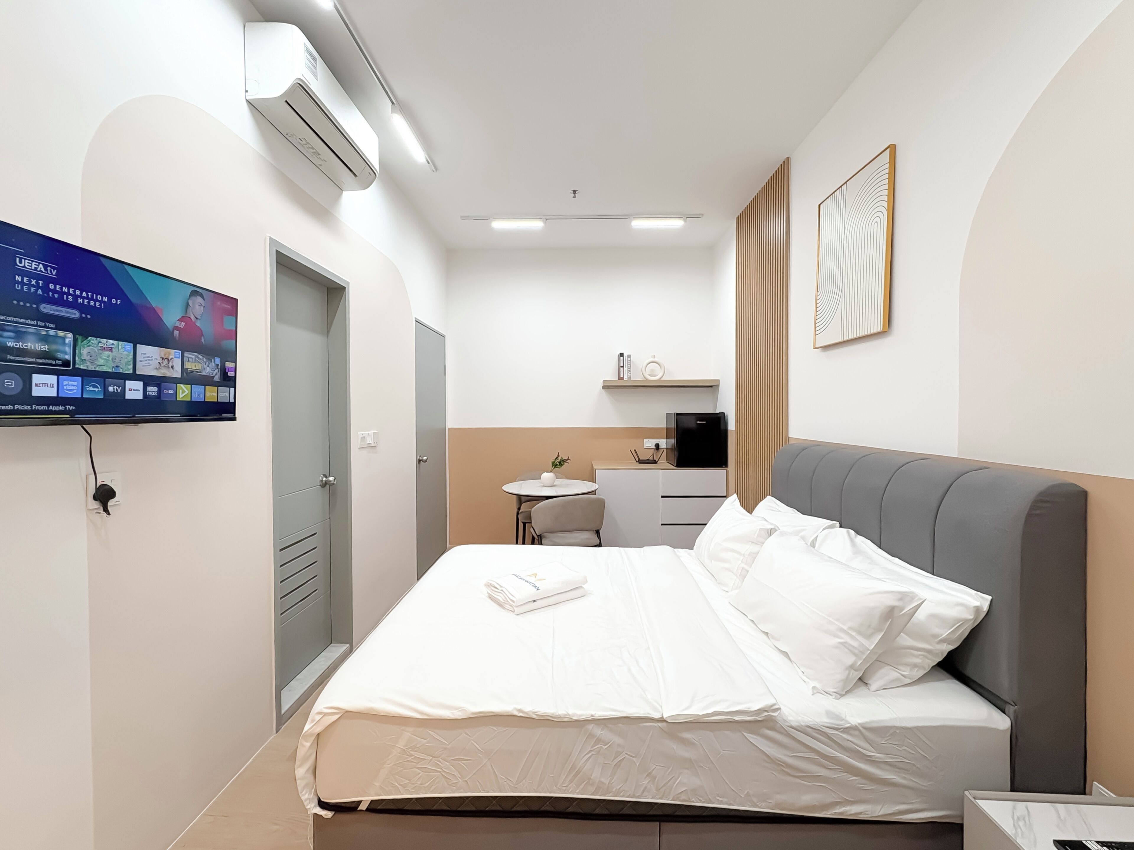 A modern hotel room with a bed, a desk, a chair, a TV, and a coffee machine.