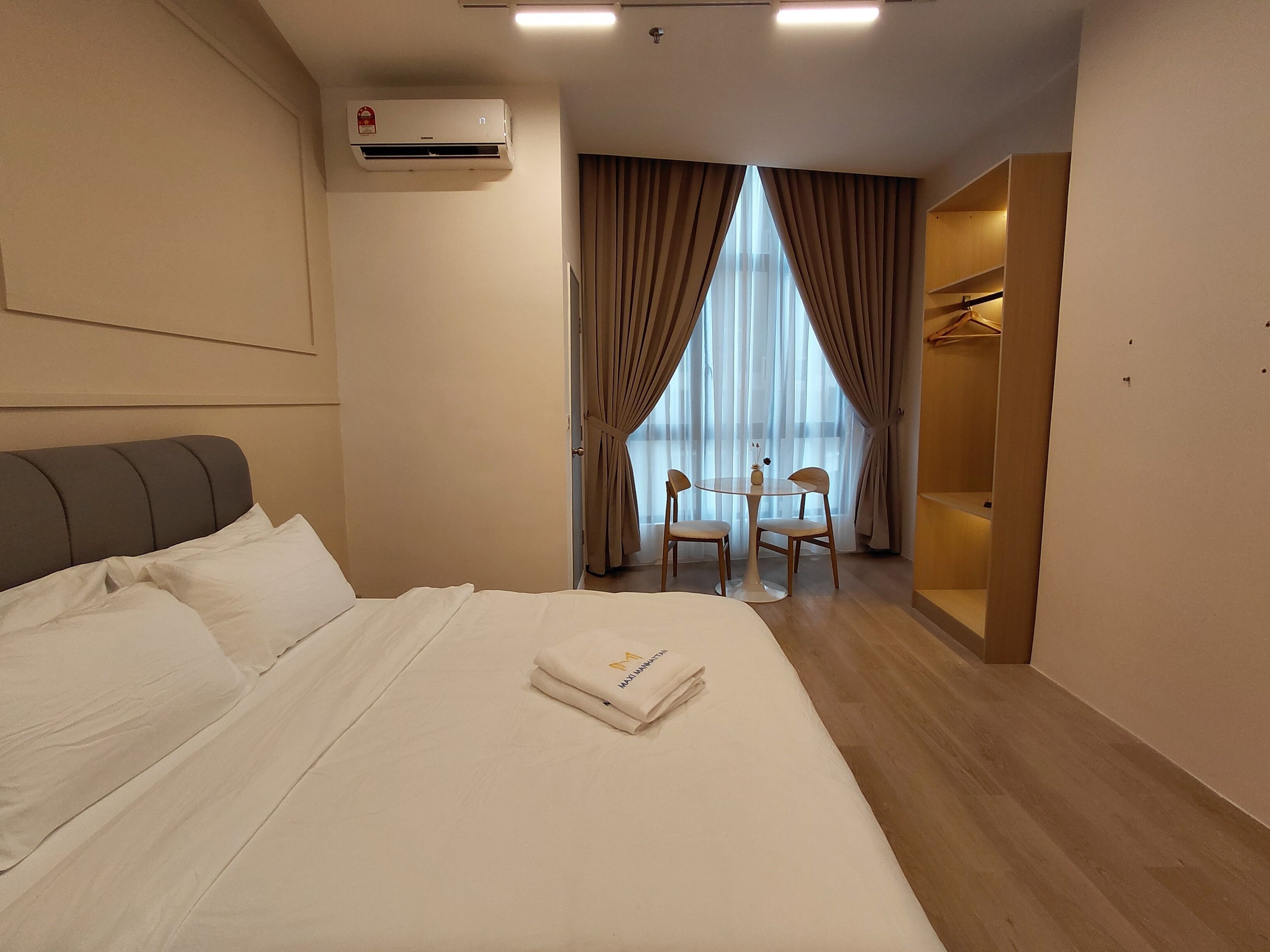 A hotel room with a bed, an air conditioning unit, a dining table with chairs, and a walk-in closet.
