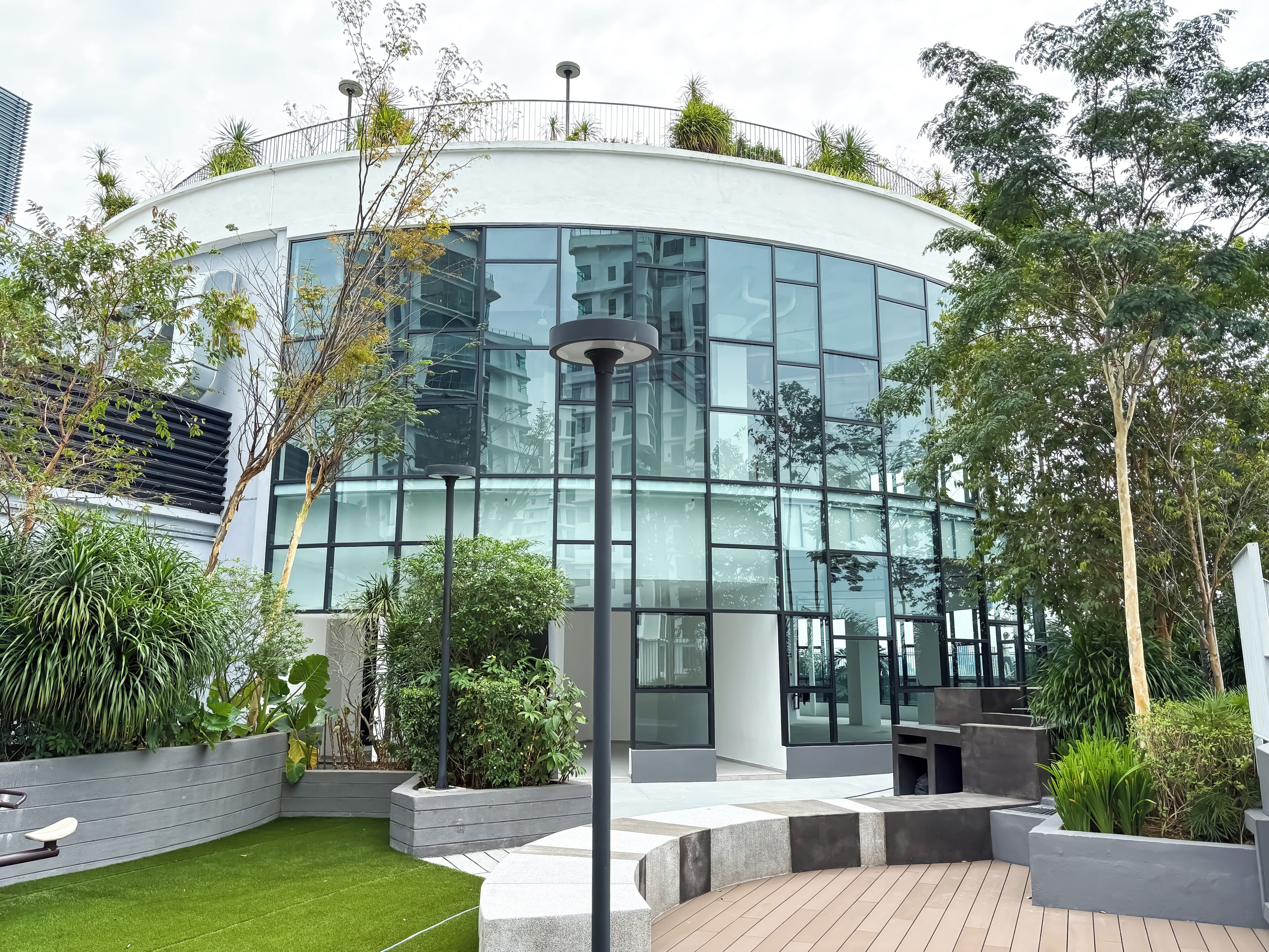 A modern building with a curved glass facade, surrounded by greenery and outdoor seating areas.