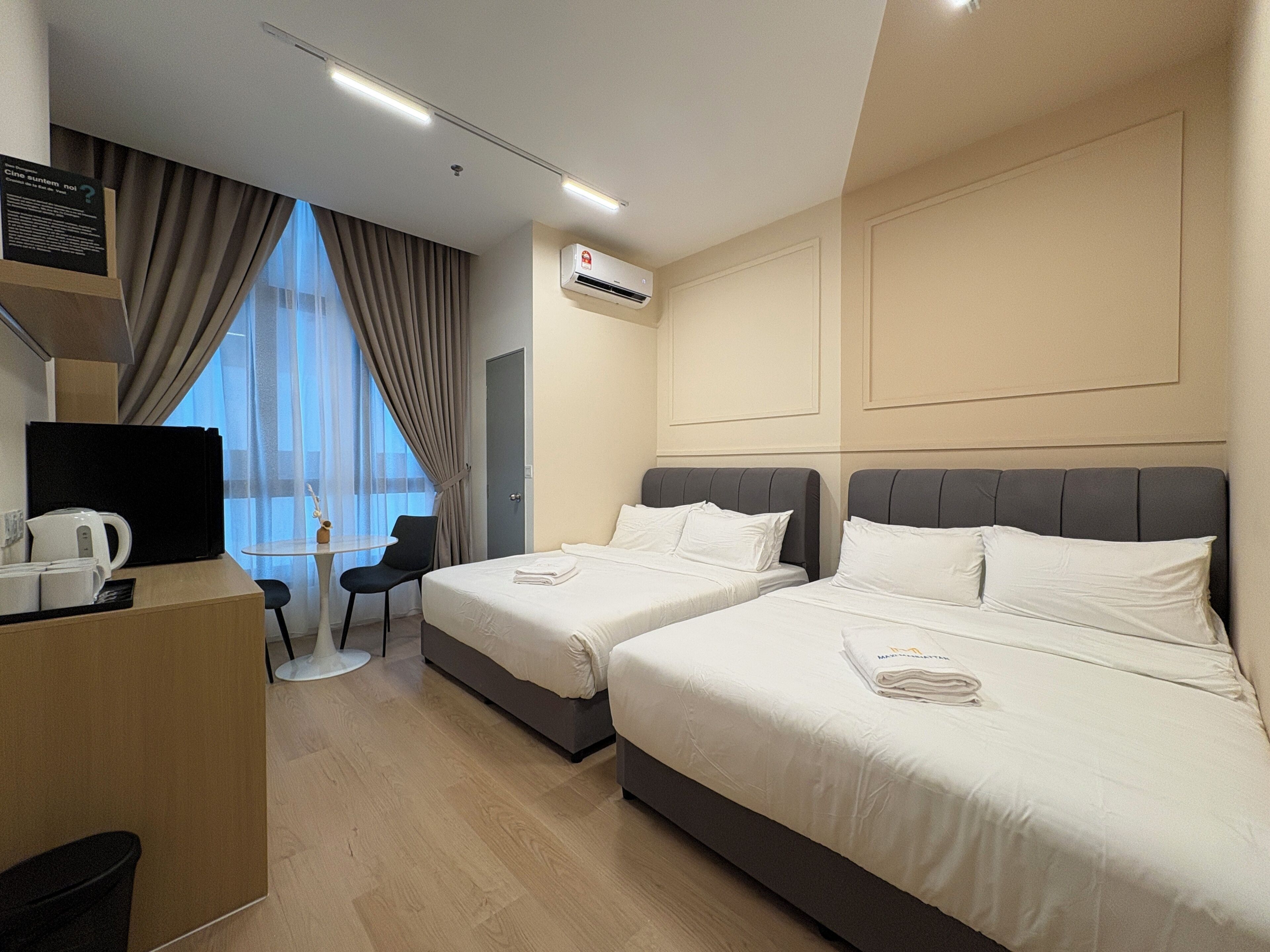 A hotel room with two beds, a desk with a coffee maker, a chair, and a view of the outside.