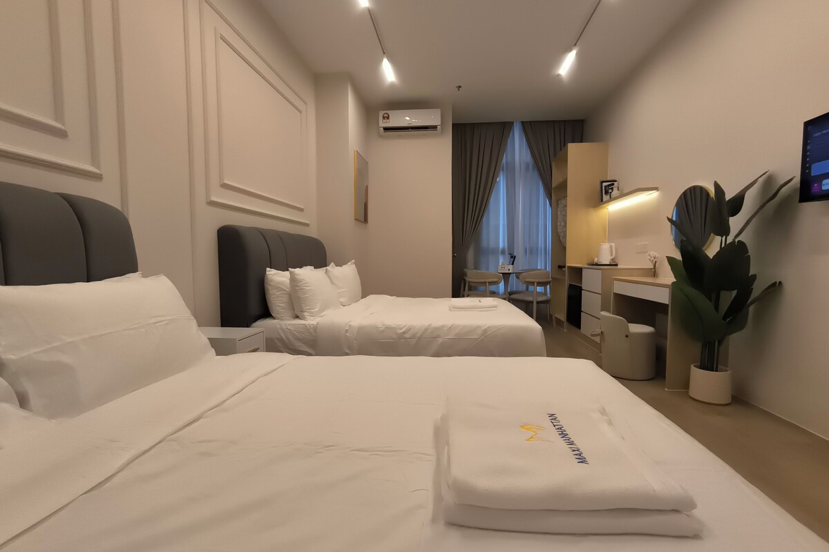 Ein Hotelzimmer mit zwei Betten, einem Schreibtisch, einem Stuhl, einer Zimmerpflanze und einer Klimaanlage.
