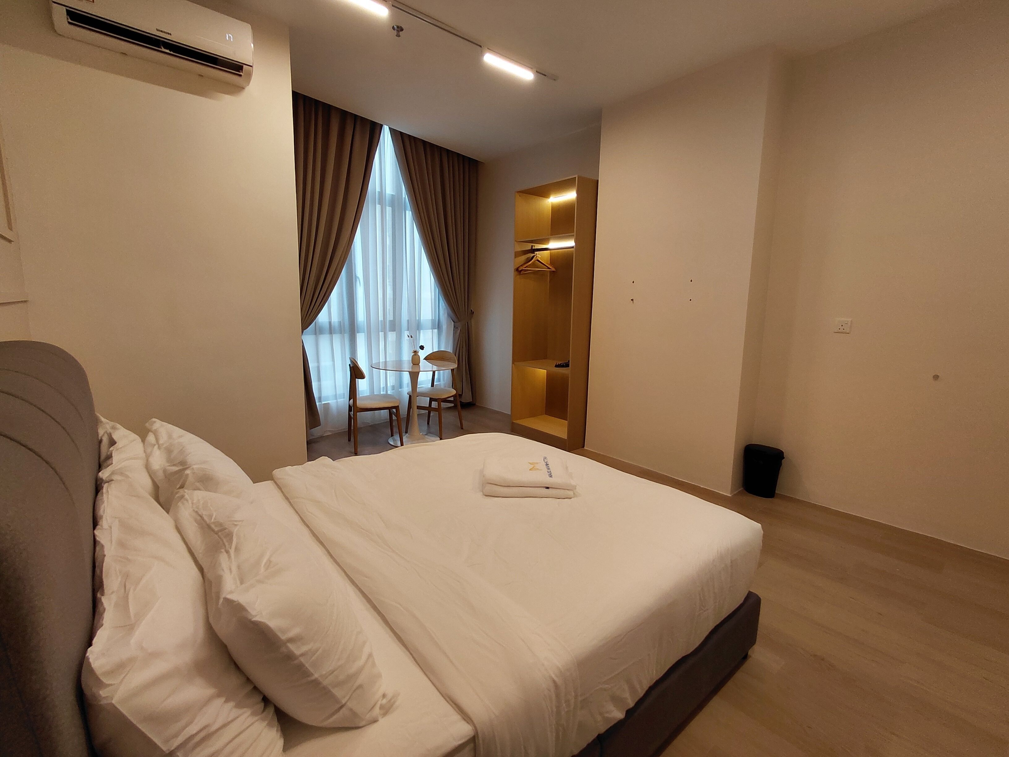 A hotel room with a bed, a small table with chairs, a wardrobe, and a window with curtains.
