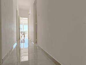 Ein sauberer, gut beleuchteter Korridor mit glänzend gefliestem Boden führt zu einem Raum mit einem großen Fenster und einem Tisch mit Stühlen.